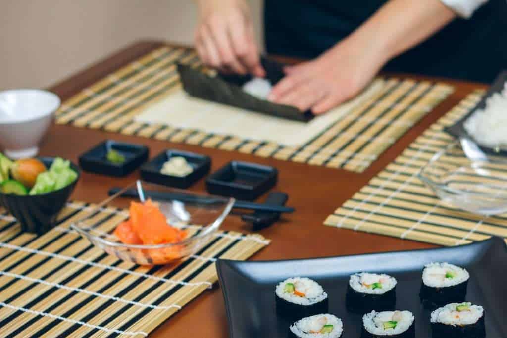 Chef hands preparing sushi with plate of finished maki rolls